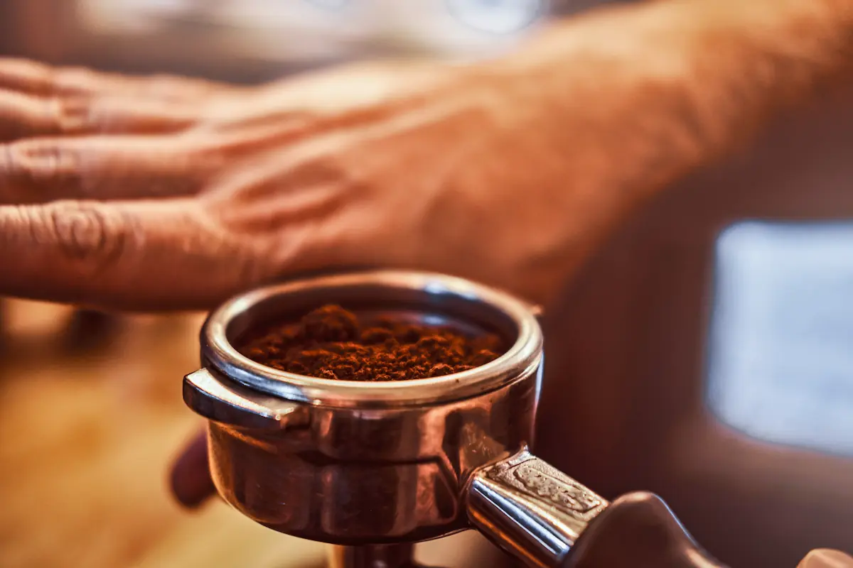 close up photo of barista hand holding portafilter with black ground coffee in cafe shop or restaurant