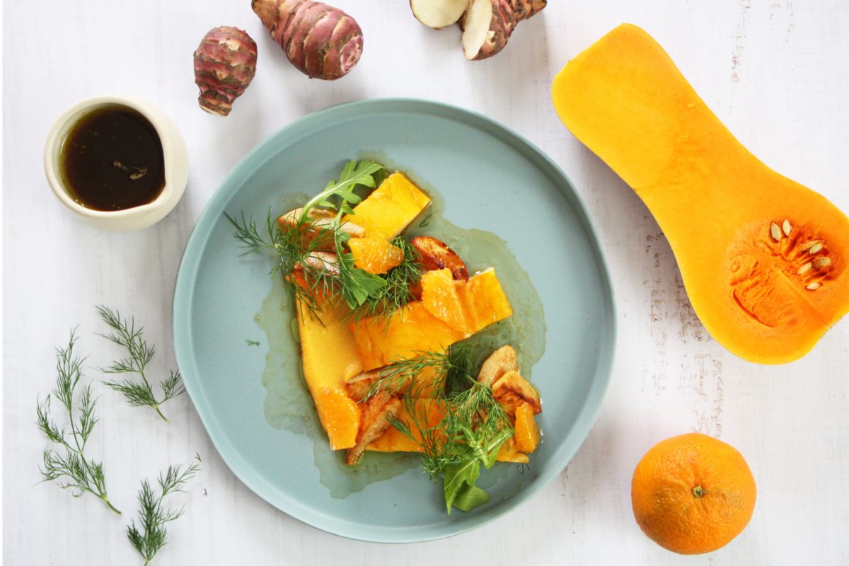une assiette de courges et d'oranges sur une table blanche, arrosée de vinaigrette.