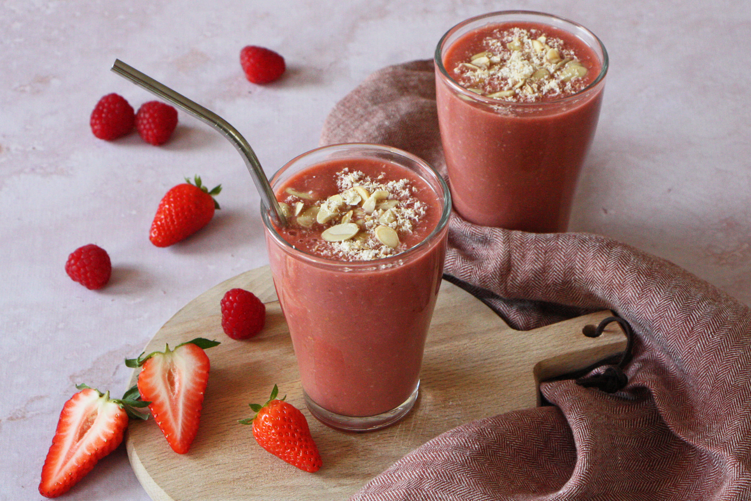 deux verres de smoothie aux fraises sur une planche à découper en bois dans un café.