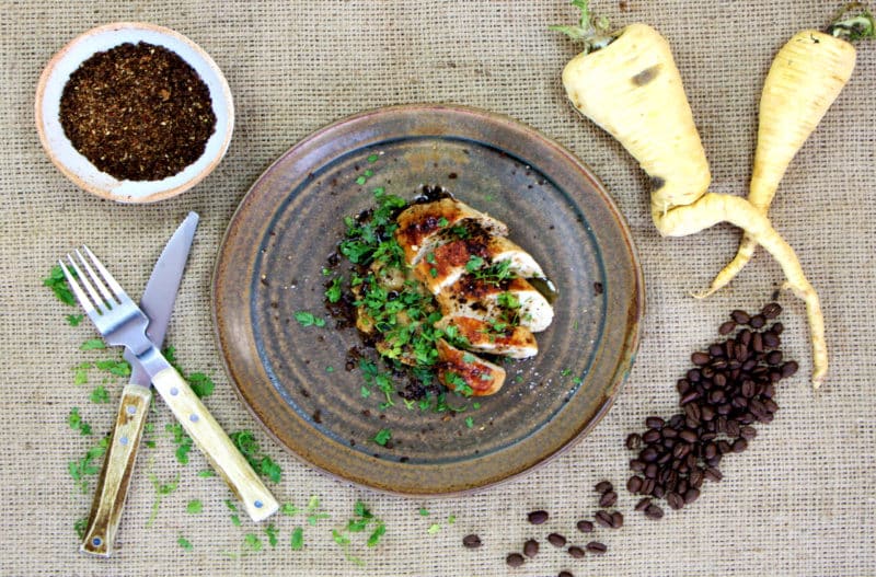 Une assiette de volaille rôtie à côté d'un couteau et d'un bol d'épices.